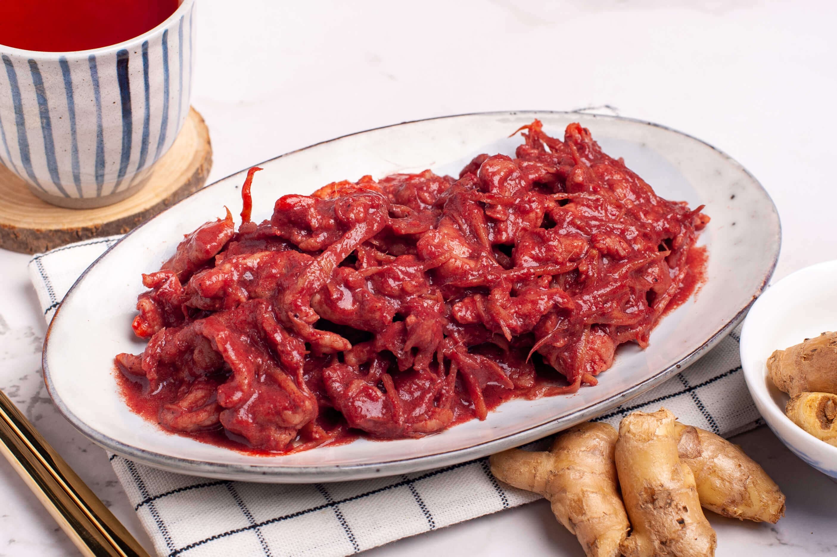Fuzhou red glutinous rice wine pork, sliced pork in a deep crimson wine sauce with shredded ginger, on an oval white plate.